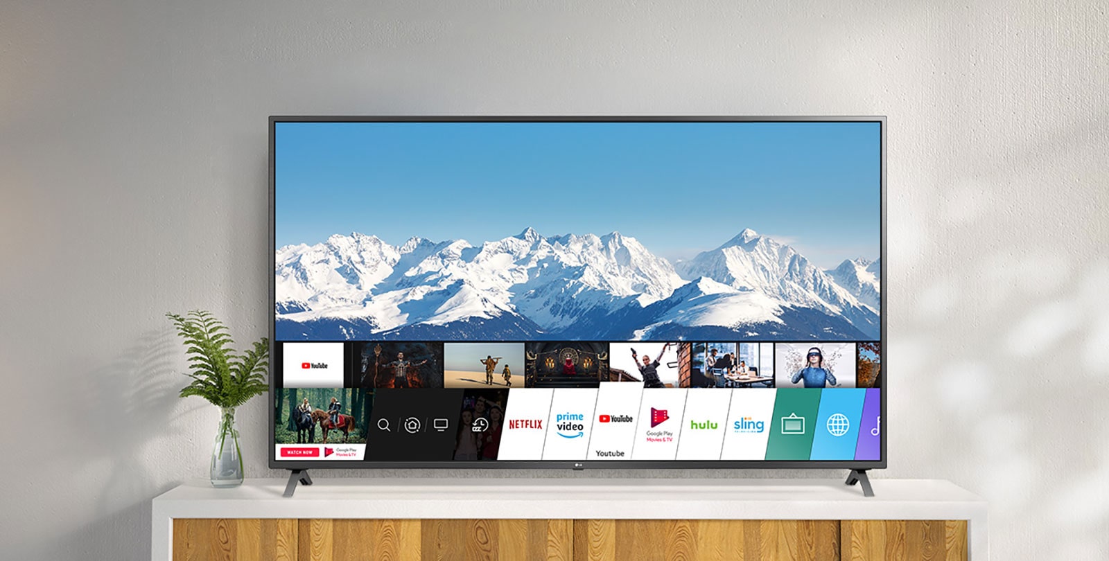 Un televisor encima de un soporte blanco contra una pared blanca. El televisor muestra la pantalla de inicio con webOS.
