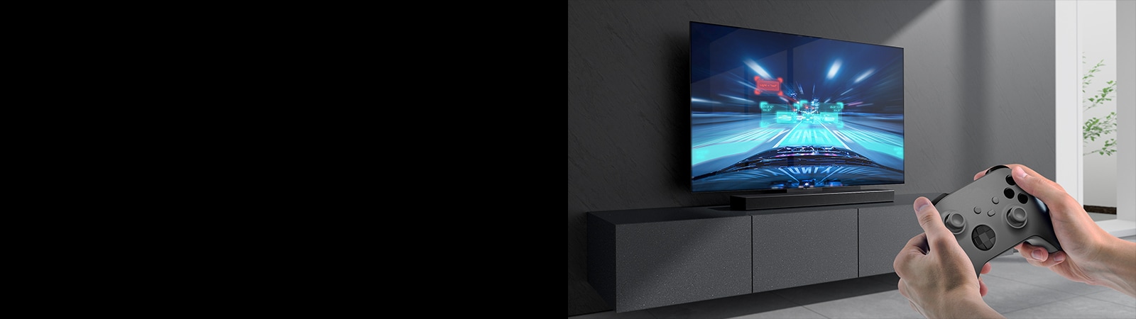La barra de sonido está colocada sobre el mueble y la escena de un juego de carreras se muestra en el televisor conectado a la barra de sonido. En la parte inferior derecha de la imagen hay una videoconsola sostenida por dos manos. 