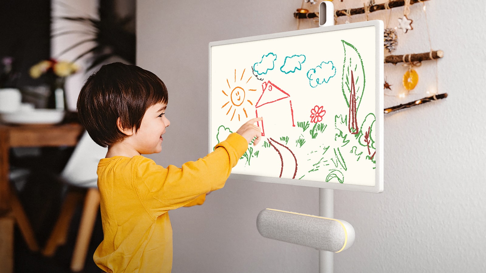 El LG StanbyME se coloca en la cocina con el altavoz XT7S conectado. Un niño dibuja en la pantalla y la iluminación ambiental amarilla del altavoz está encendida.