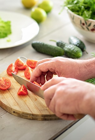 Image of cutting tomatoes on a cutting board with a knife.