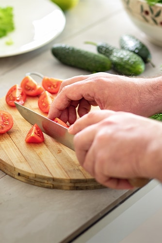 Image of cutting tomatoes on a cutting board with a knife.