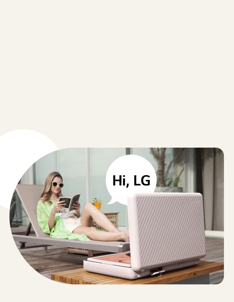 Vista trasera del LG StanbyME Go, colocado justo delante de la mesa del patio. Una mujer se relaja en la silla de playa y controla la pantalla con su voz. Para ilustrarlo, a su derecha aparece una burbuja de voz con el texto "Hi LG".