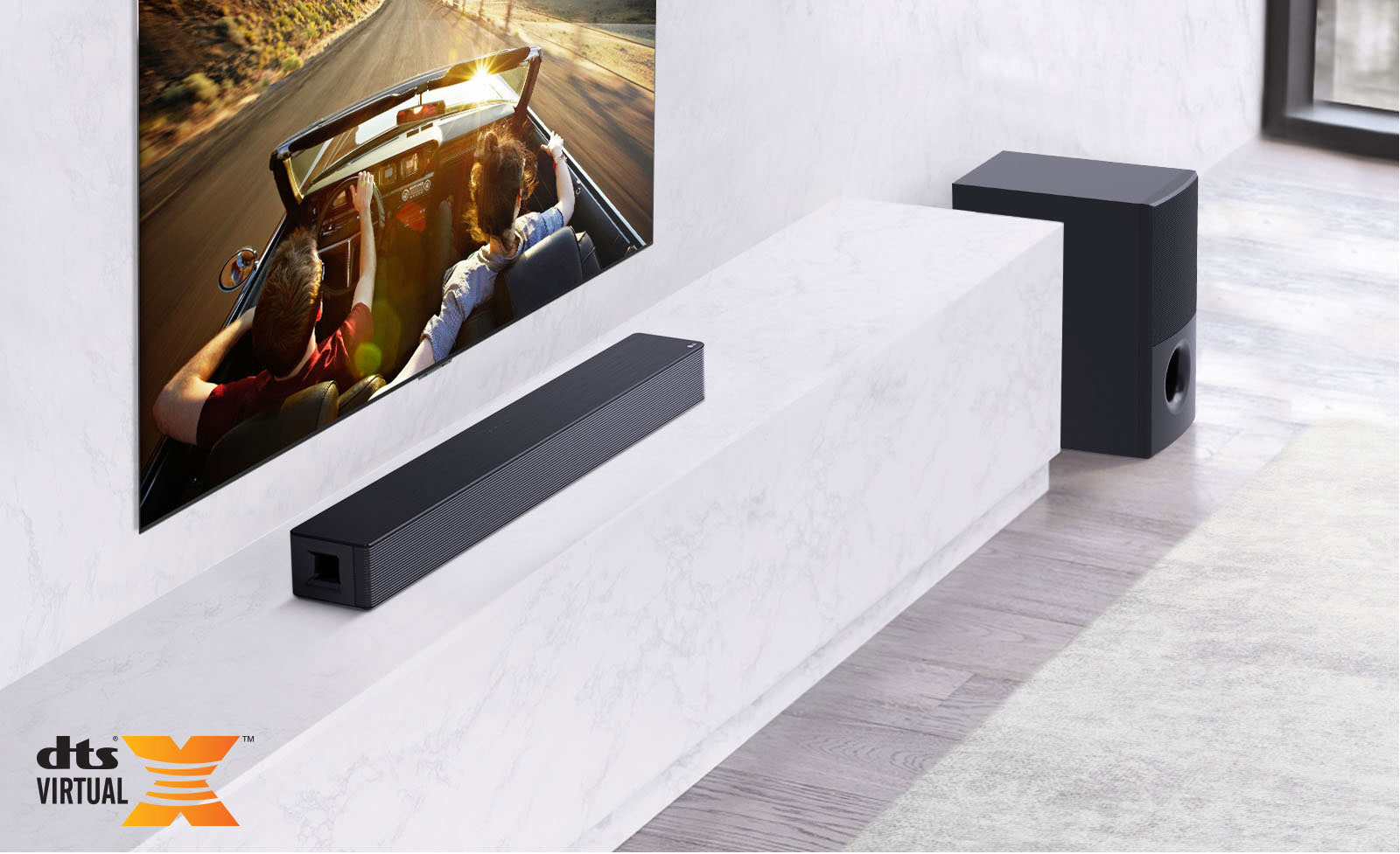 El televisor está instalado en la pared, la barra de sonido LG está debajo encima de un estante de mármol blanco con un subwoofer a la derecha. El televisor muestra una pareja en un coche.