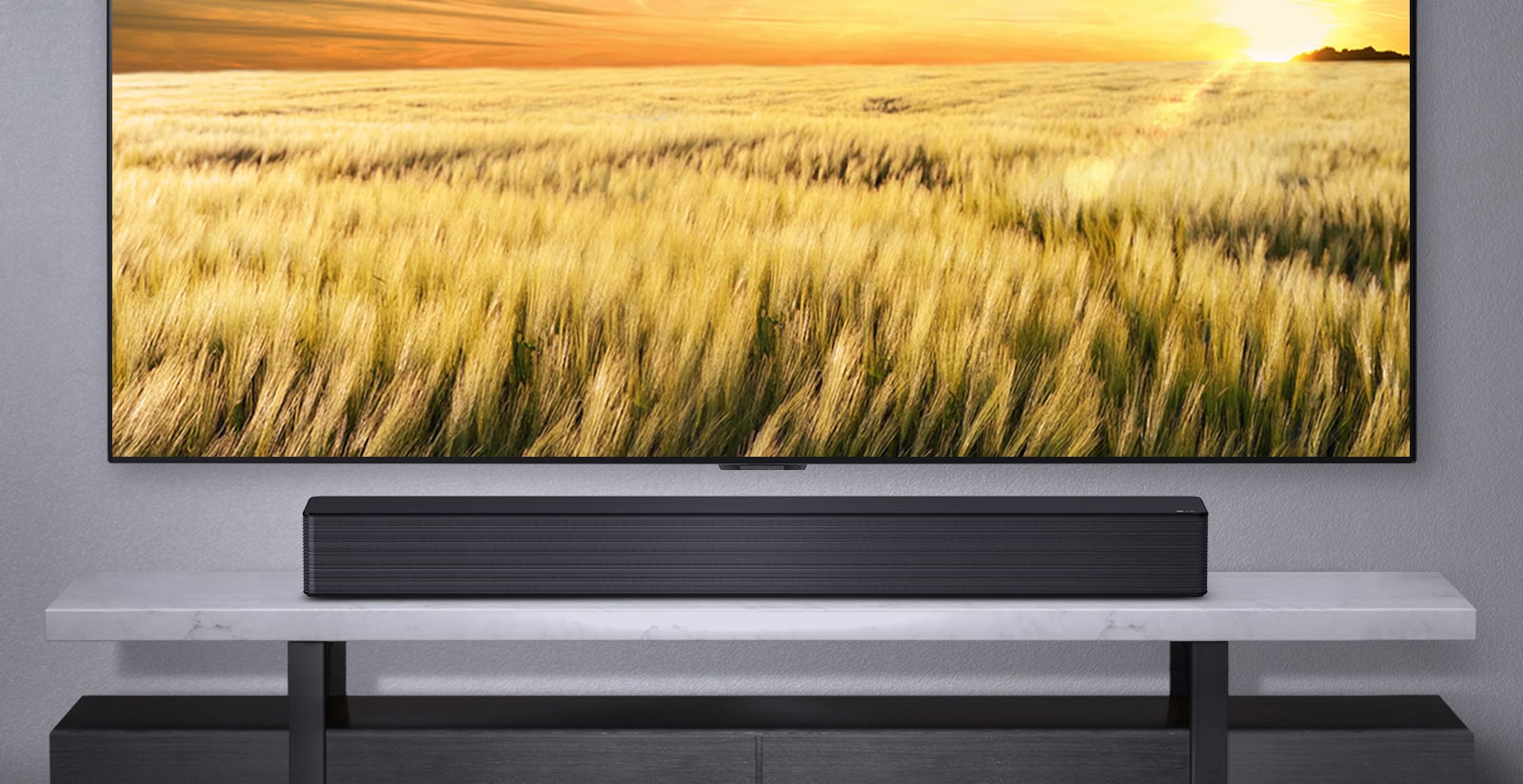 Se muestra un televisor en una pared gris y la barra de sonido LG debajo de un estante gris. Disco Blue-Ray debajo del estante.