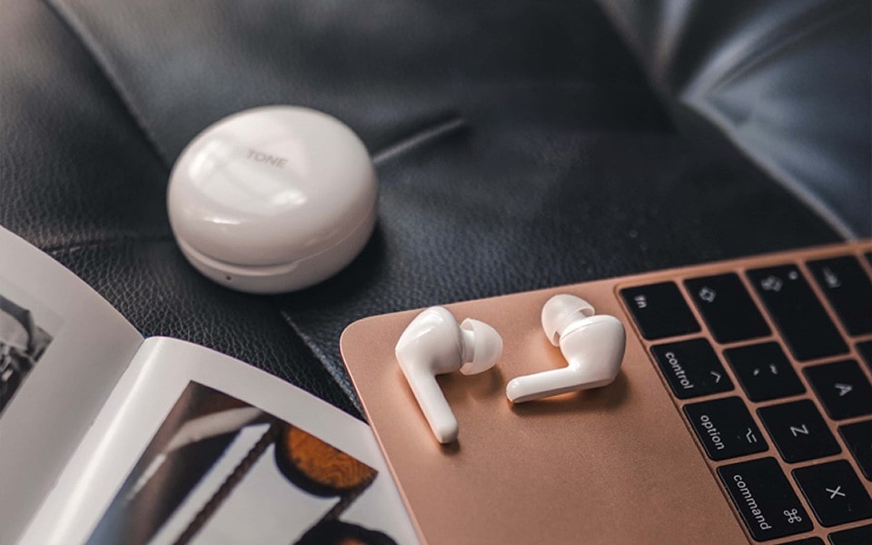 A pair of earbuds lays on top of a laptop with a charging cradle nearby