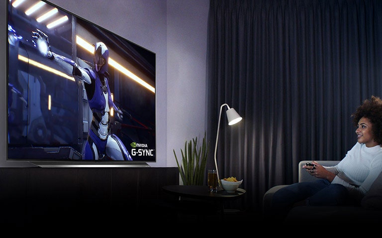 Nainen istuu sohvalla ja käyttää peliohjainta ja pelaa peliä tv-ruudulla