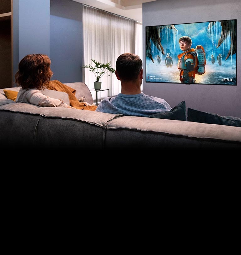 Olohuoneen sohvalla istuu pariskunta katsomassa romanttista elokuvaa televisiosta