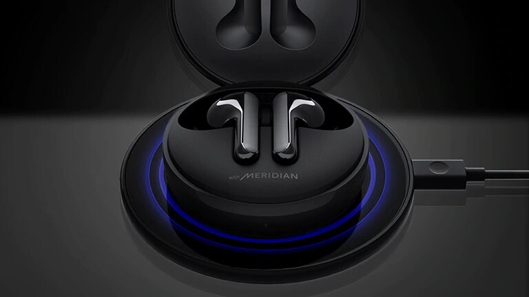 Kuva mustista LG TONE Free FN6 -nappikuulokkeista avatussa kotelossa mustan langattoman latauslevyn päällä, jossa on sininen valo 