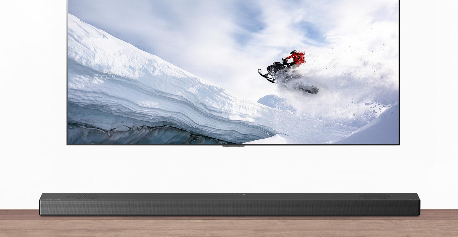 Televisio ja soundbar-kaiutin edestäpäin. Televisiossa mies ajaa lumikelkalla lumisilla vuorilla. HDMI 2.1 -logo television alapuolella. 