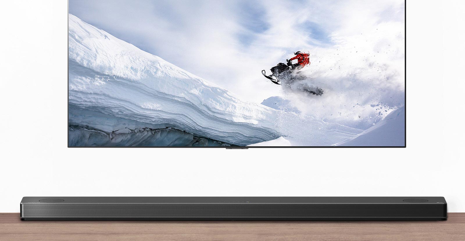Televisio ja soundbar-kaiutin edestäpäin. Televisiossa mies ajaa lumikelkalla lumisilla vuorilla. HDMI 2.1 -logo television alapuolella. 