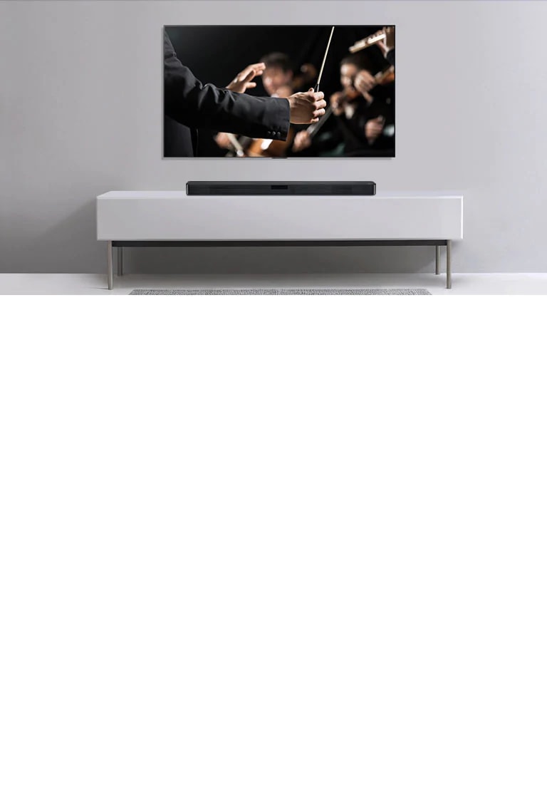 Harmaalla seinällä on televisio ja sen alla harmaalla tasolla on LG-soundbar-kaiutin. Televisiossa kapellimestari johtaa orkesteria.