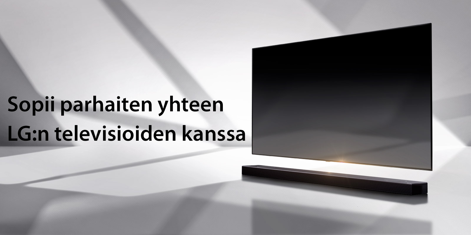 Soundbar-kaiutin ja TV ovat valkoisella lattialla ja ulkoa oikealta takaa tulee varjo.