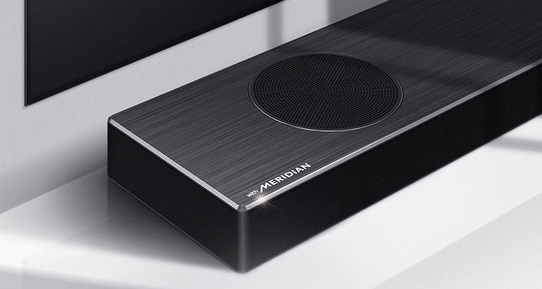 Lähikuva LG Soundbar -kaiuttimen vasemmasta reunasta, jonka vasemmassa alakulmassa näkyy Meridian-logo. Television vasen alareuna on myös näkyvissä. 