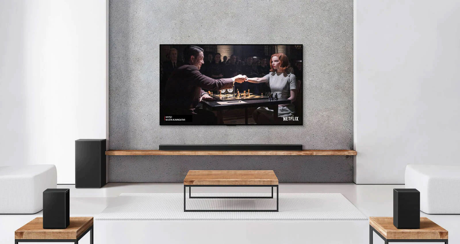 Kaksi takakaiutinta, alabassokaiutin, soundbar-kaiutin ja TV ovat valkoisessa olohuoneessa Nainen ja mies pelaavat shakkia TV-ruudulla.