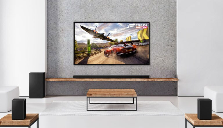 Kaksi takakaiutinta, alabassokaiutin, soundbar-kaiutin ja TV ovat valkoisessa olohuoneessa TV-ruudulla ajava auto ja avaruusalus 