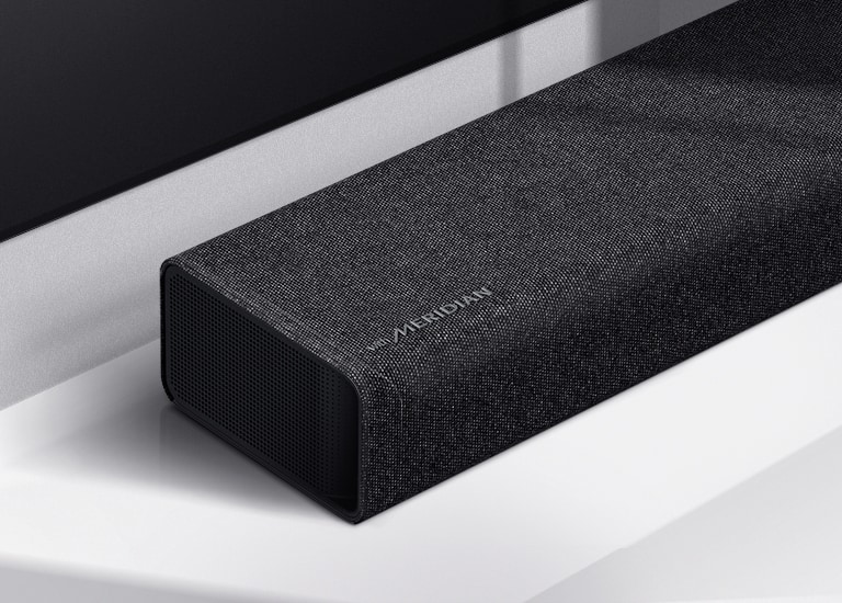 Lähikuva LG Soundbar -kaiuttimen vasemmasta reunasta, jonka vasemmassa alakulmassa näkyy Meridian-logo. Television vasen alareuna on myös näkyvissä.