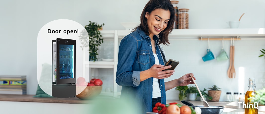 Kuva naisesta laittamassa ruokaa ja katsomassa puhelintaan ja jääkaapista, jonka ovi on auki.