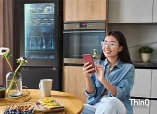 Kuva naisesta, joka koskettaa puhelintaan keittiössä.