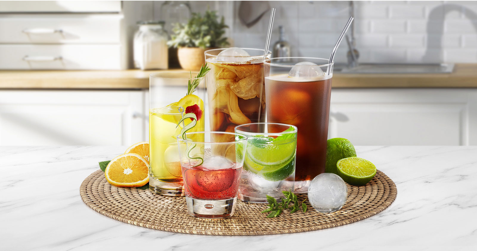 Various glasses of different sizes holding different drinks with round ice cubes are on a kitchen counter.