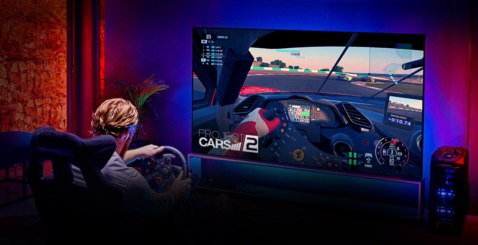 Man in a dark room sitting on a racing game seat in front of a large TV playing a racing game (scroll down the page)