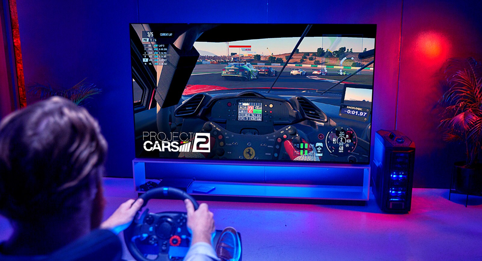 Back shot of a man in front of a large TV playing a racing game 