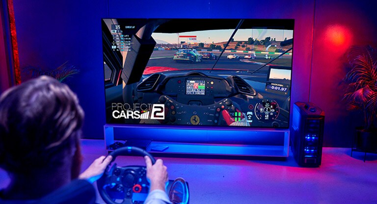 Back shot of a man in front of a large TV playing a racing game 