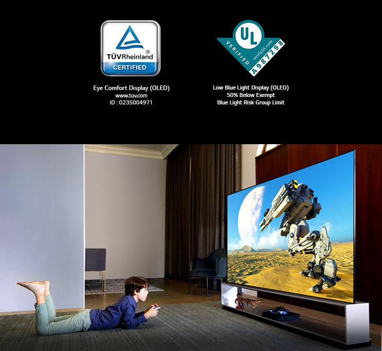 Boy lying on his stomach in front of a large TV with controllers in his hands,