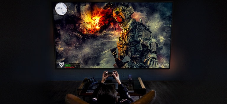 Back shot of a boy playing a war game in front of a large screen TV