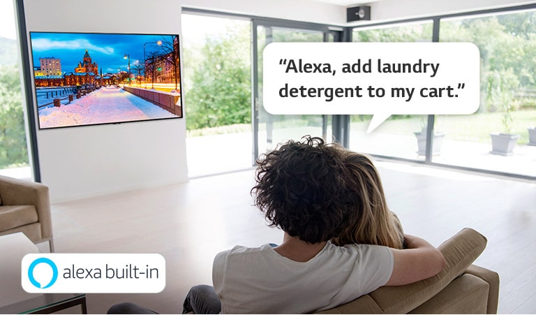 Pariskunta istuu sohvalla ja pyytää Amazon Alexaa lisäämään pyykinpesuaineen ostoskärryyn