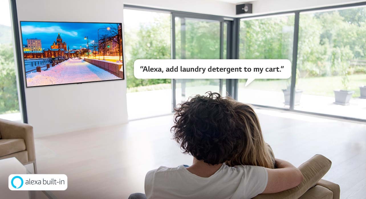 Pariskunta istuu sohvalla ja pyytää Amazon Alexaa lisäämään pyykinpesuaineen ostoskärryyn