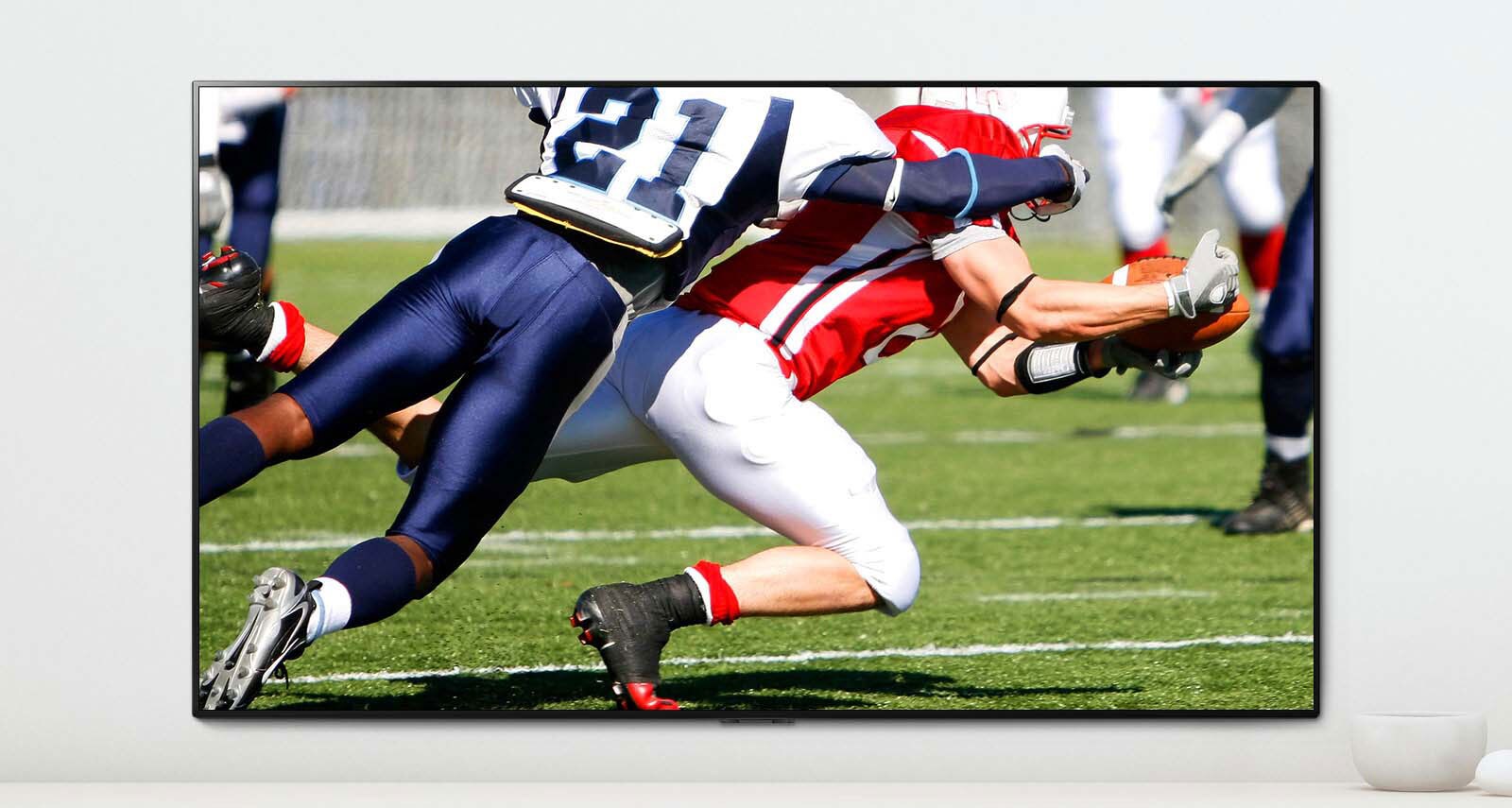 Kohtaus urheilupelistä, jossa kaksi miestä pelaa dynaamisesti amerikkalaista jalkapalloa TV-ruudulla.