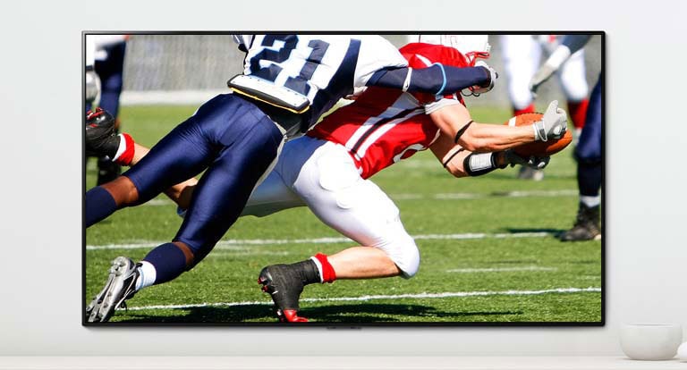 Kohtaus urheilupelistä, jossa kaksi miestä pelaa dynaamisesti amerikkalaista jalkapalloa TV-ruudulla.