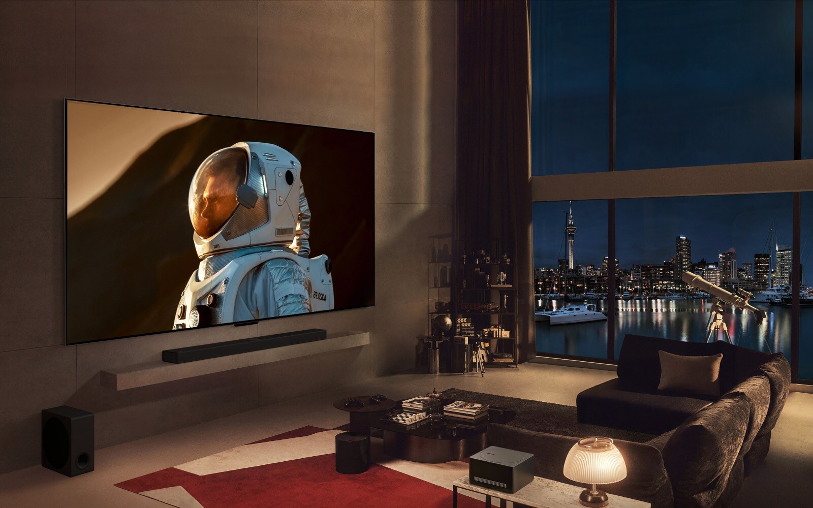 Erittäin suuri LG TV on asennettu kotoisan olohuoneen seinälle. Näytöllä, joka peittää suurimman osan seinästä, näkyy lähikuva astronautista. Mies istuu sohvalla katselemassa televisiota koiran kanssa, ja ikkunasta näkyy öinen kaupunkimaisema.