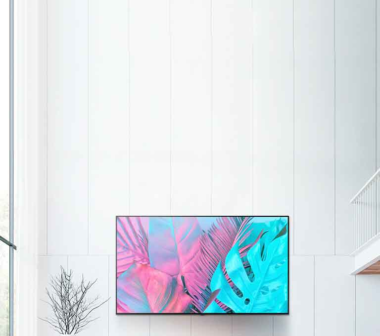Suuri taulu-tv kiinnitettynä valkoiselle seinälle. Näytössä näkyy suuria lehtiä kirkkaissa väreissä.