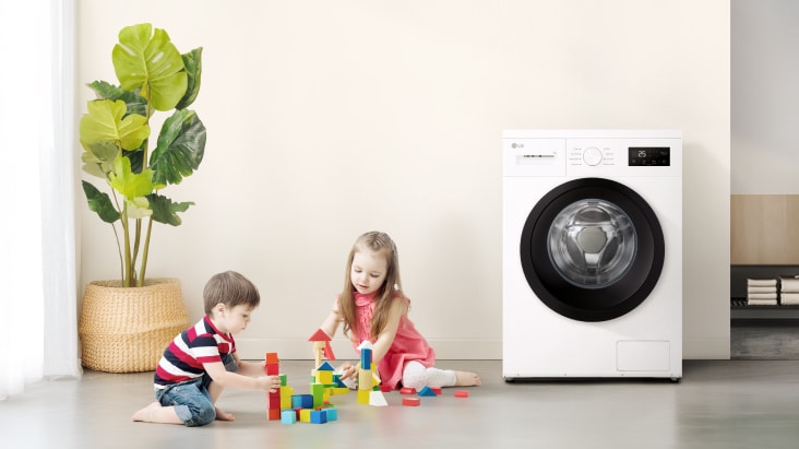 Kaksi lasta leikkimässä värikkäillä leluilla pesukoneen lähellä