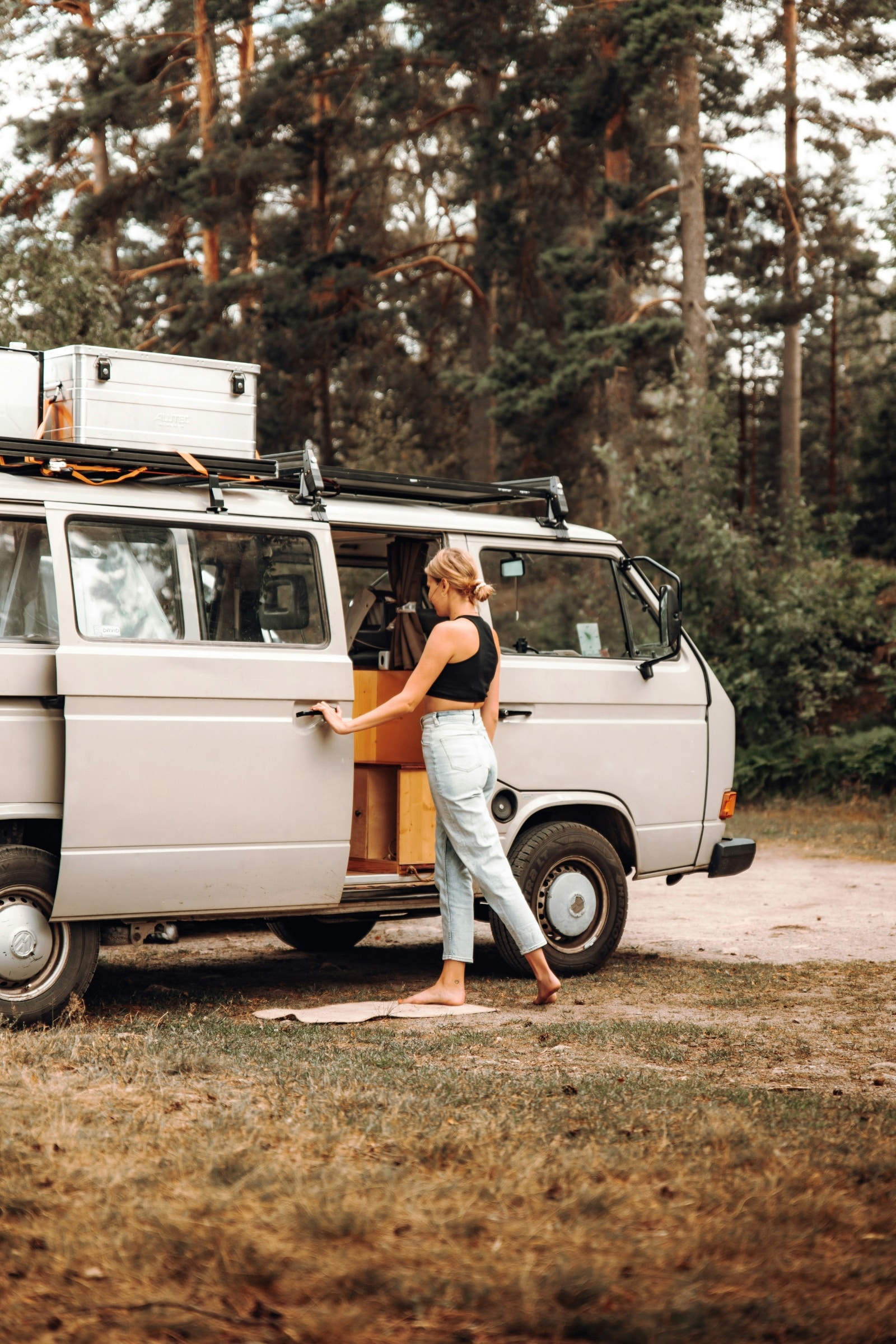  Une femme ouvre la porte coulissante d’un camping-car vintage garé dans une forêt.