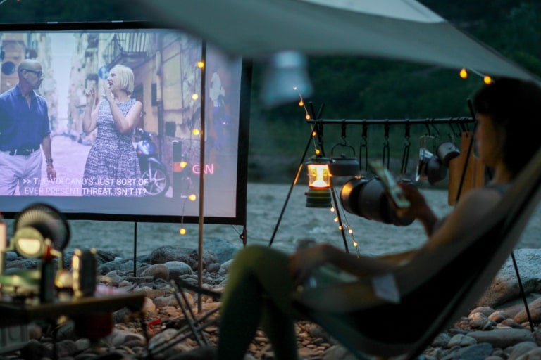 Une personne allongée dans une tente rouge, écoutant de la musique et profitant de la nature, gadgets de camping pour une expérience en plein air optimale.