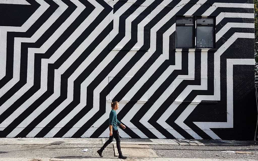 Voyager à Berlin : Un homme passe à côté du Street Art noir et blanc des rues de Berlin.