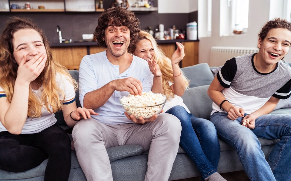 An image of four friends watching LG TV joyfully and eating popcorn.