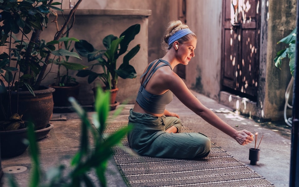 An image of a woman sitting on the floor to meditate as she lights her incense burner.