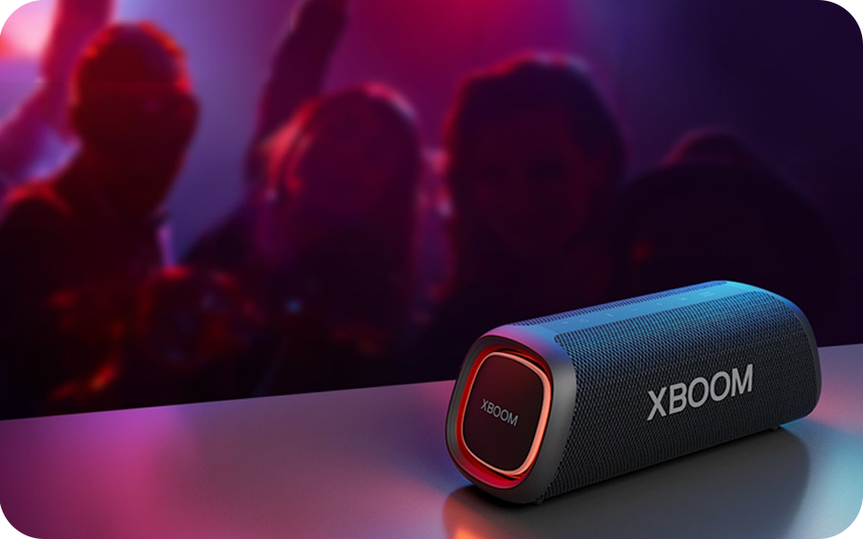 LG XBOOM Go XG5QBK portable Bluetooth speaker on a table with party lights and lively atmosphere in the background