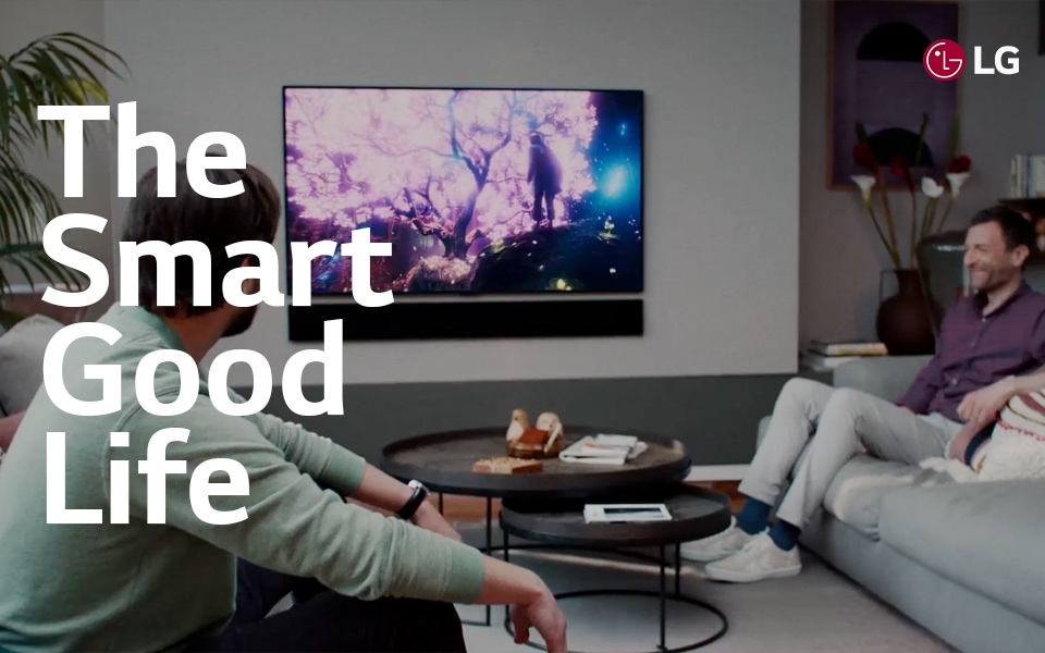 An image of a living room with two men sitting looking at the LG OLED tv and text that reads "The Smart Good Life".