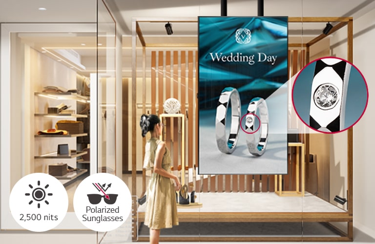 A woman wearing sunglasses is watching ads on the display installed in a shop window, and the ads on the display are very visible even under the strong sunlight.