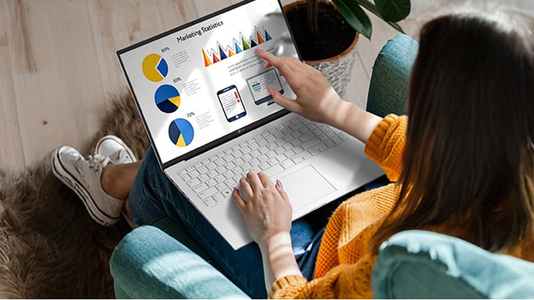 The image shows a person using a laptop while seated comfortably, interacting with the touchscreen to navigate charts and graphs. An animation demonstrates the anti-glare screen by showing no light reflection even when sunlight shines directly onto the display.