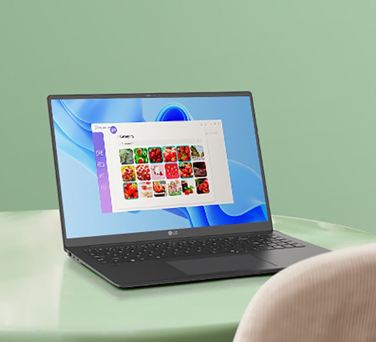 A laptop placed on a green table, displaying a gallery application interface with images of red fruits on the screen, suggesting navigation or photo management activities.	