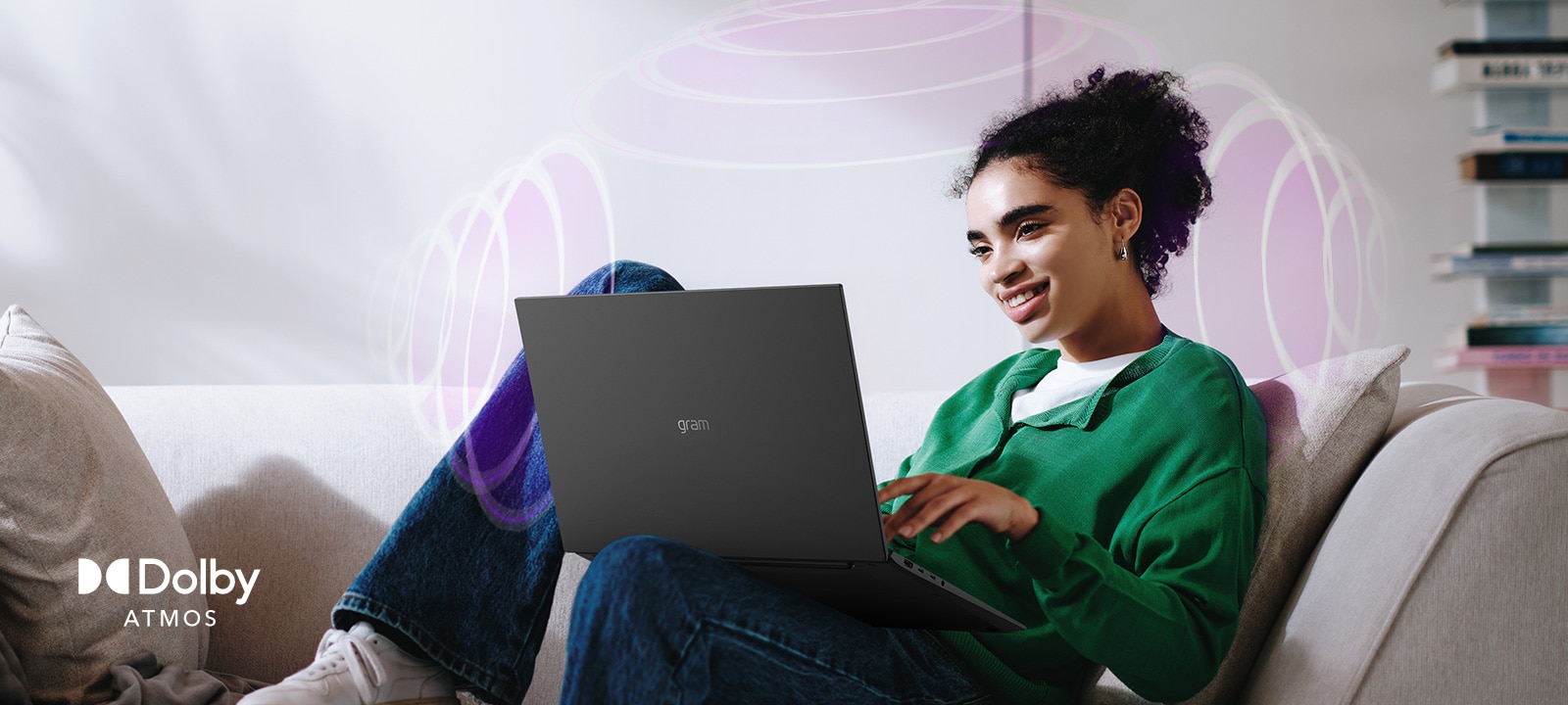 A person sitting on a couch, enjoying immersive audio while using an LG gram laptop. The text highlights Dolby Atmos technology, emphasizing a rich, expansive, 360-degree auditory experience. Surrounding sound waves in the background visually represent the immersive soundscape.	