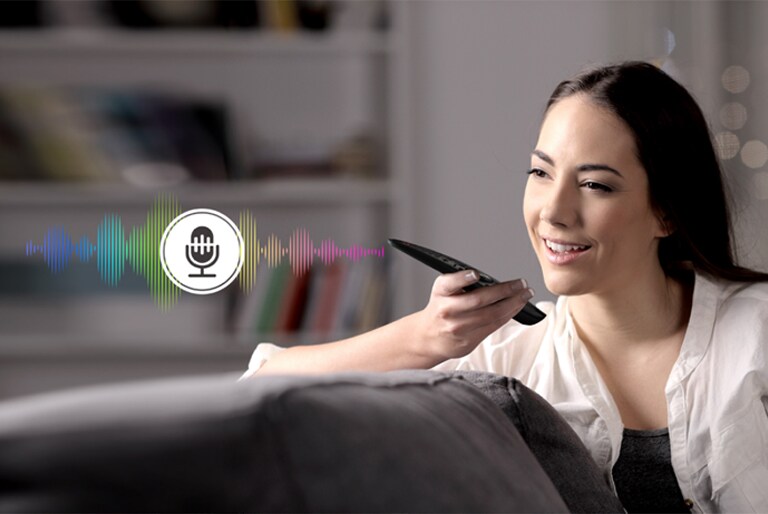 A woman is controlling TV by speaking to a remote control which has voice recognition.