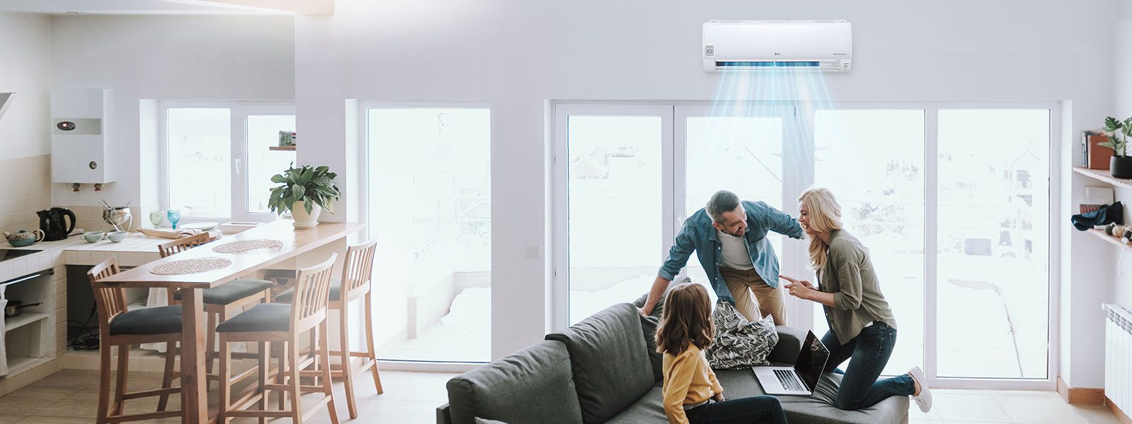 A wall-mounted air conditioner supplying blue-colored air stream in a living room while three family members smiling at each other on a sofa. 