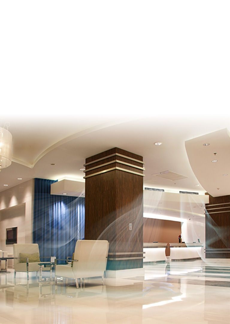 A ceiling concealed duct supplying blue-colored air current in a large hotel lobby with high ceiling, tall brown pillars and ivory-toned sofas.