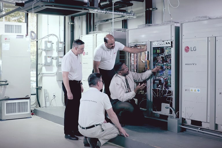Four experts inspect an LG MULTI V i unit installed by the wall, checking its performance and key components.